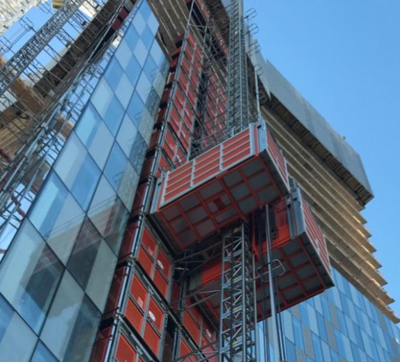 An exterior view of a skyscraper under construction, featuring a red and gray elevator shaft, a large windowed wall, and a...