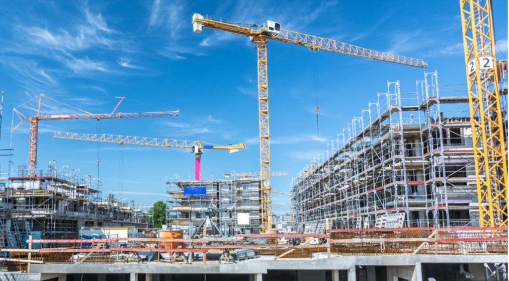 A construction site with multiple cranes and scaffolding under a blue sky.