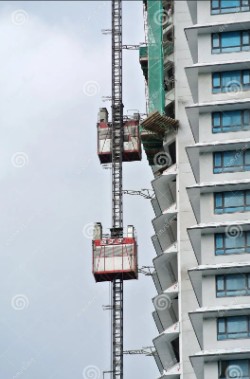 A tall building with a fire escape ladder and a red basket lift, set against a gray sky.