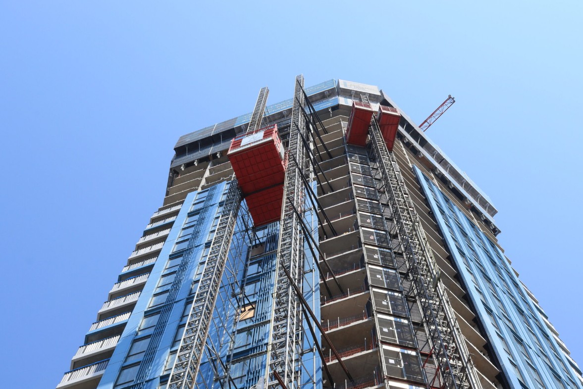 A tall building under construction, with scaffolding and cranes visible, set against a clear blue sky.